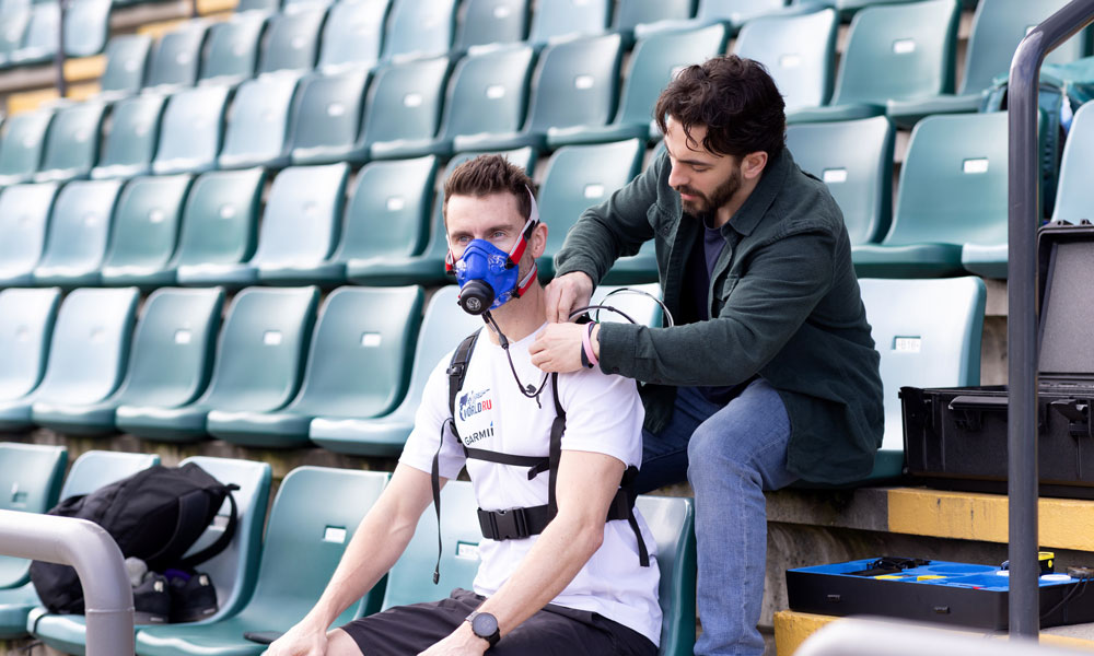 Researcher Nate Adams fits athlete Mike Shaw with a portable VO₂ mask and sensors in an empty stadium